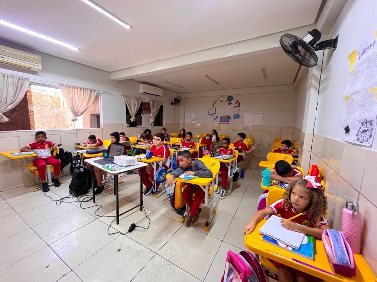Sala de aula da CEDEF cheia de alunos de uniforme vermelho em carteiras amarelas